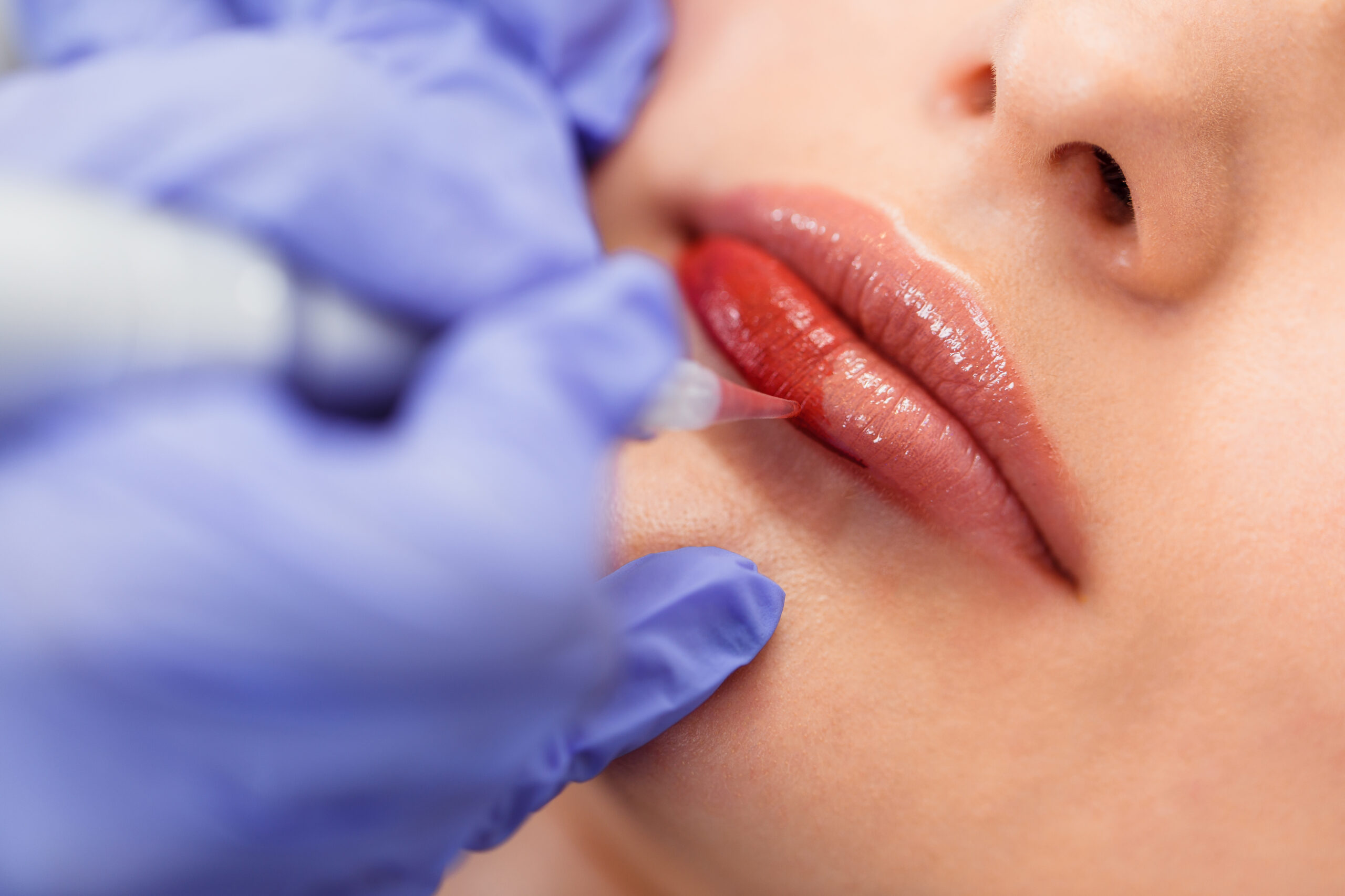 Young woman having permanent makeup on lips in beautician salon.