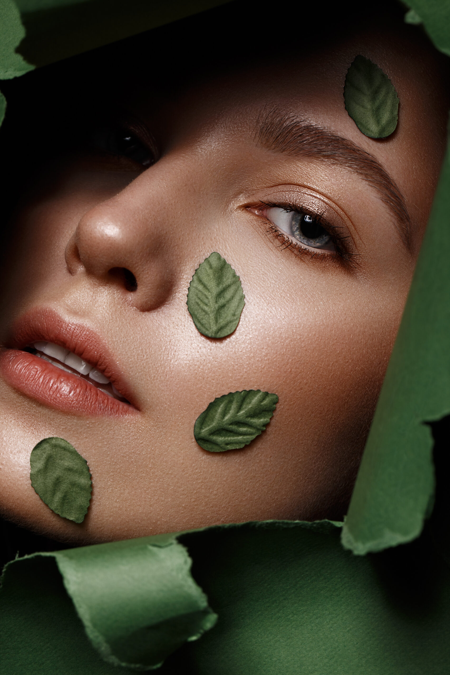 Beautiful fresh girl with perfect skin, natural make-up and green leaves. Beauty face. Photo taken in the studio.