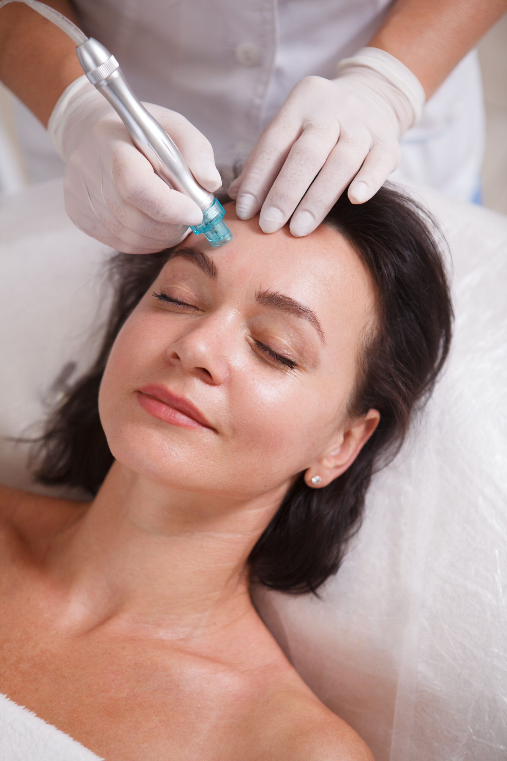 Vertical close up of a woman enjoying hydra pores cleaning procedure by cosmetician